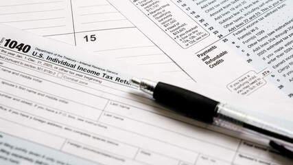 Fototapeta premium Person filling out a 1040 tax form with a pen on a desk, close-up representing annual us income tax filing and paperwork