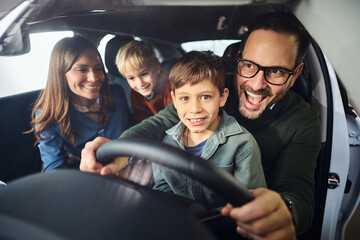Happy family having fun while testing new car in showroom.