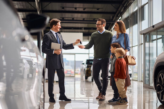 Happy family receiving key of their new car in showroom.
