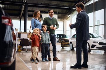 Happy parents with kids communicating with car salesperson in showroom.