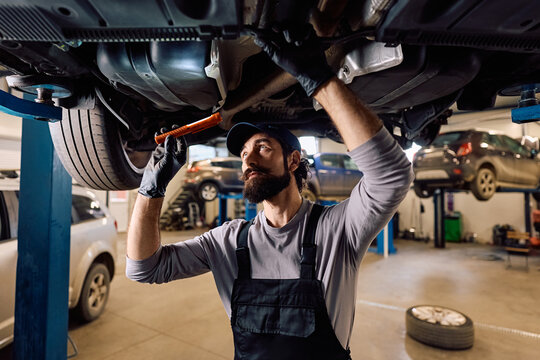 Car mechanic doing maintenance on chassis while working in garage.