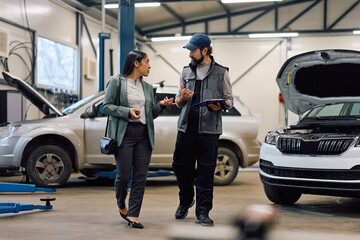 Mid adult woman talking to mechanic about her car problems in repair shop.