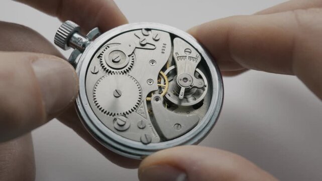 Hands hold a silver pocket watch, revealing the internal mechanical movement. The balance wheel oscillates and gears turn. This concept illustrates precision engineering and vintage timekeeping