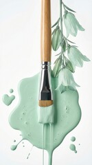 Paintbrush resting on mint green paint with delicate flowers
