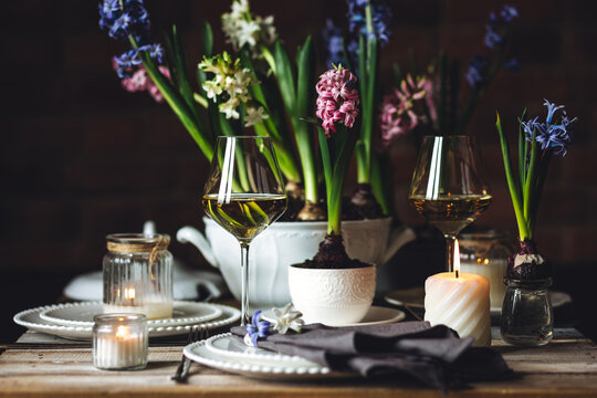 Beautiful elegant table setting for Easter celebration with fresh spring hyacinth flowers, burning candles. Romantic wedding dinner table decoration. Springtime, home gardening. Dark background