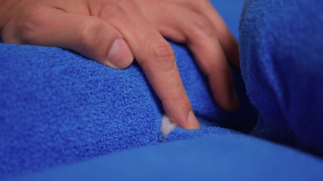 Close examination of torn sofa upholstery. Adult hand explores tear in fabric for repair. Detailed scene showing fingers probing fabric damage on sofa for repair