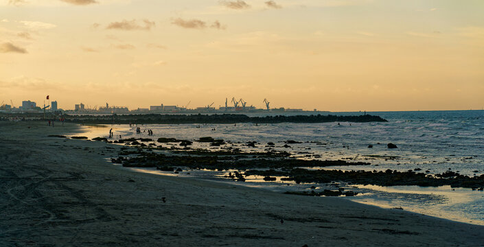 Sunset Over The Sandy Coast And Distant Port Cranes