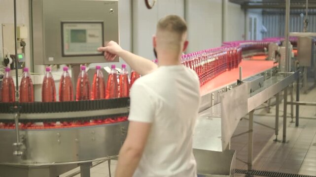 Factory worker operating touch screen control panel on automated bottling production line.
