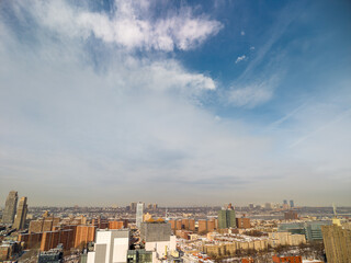 New york city cityscape featuring diverse buildings, high rise towers, and residential blocks under a partially cloudy blue sky, captured during winter with traces of snow on rooftops