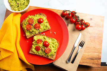 Plant-based avocado toast topped with cherry tomatoes and diced onion, photographed from above in a modern kitchen setting. The vibrant colors and minimal styling highlight fresh ingredients and conte