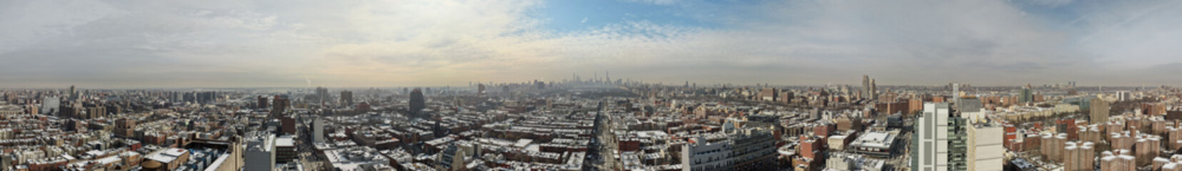 Obraz premium Panoramic aerial view of manhattan skyline and extensive new york city urban sprawl, snow dusted rooftops and streets in winter creating a cold, dramatic cityscape