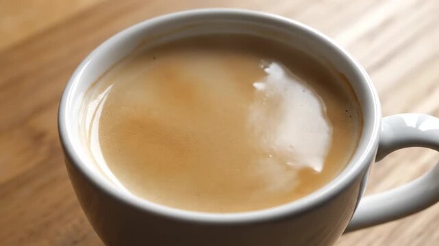 Cup of coffee with settling foam. A cup of freshly poured coffee shows foam gradually settling as bubbles shrink and disappear.