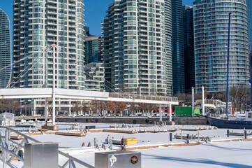 Fototapeta premium Toronto harbourfront marina frozen and blanketed with snow and ice, waterfront condominiums and a pedestrian bridge rising against a clear blue winter sky over lake ontario