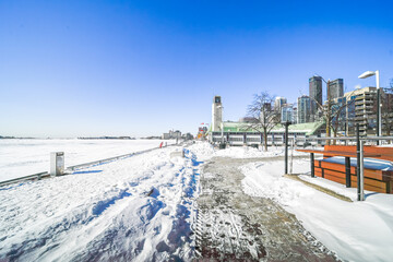 Obraz premium Toronto harbourfront centre blanketed in snow under a clear blue sky, overlooking the frozen expanse of lake ontario with skyline, park paths and serene winter cityscape
