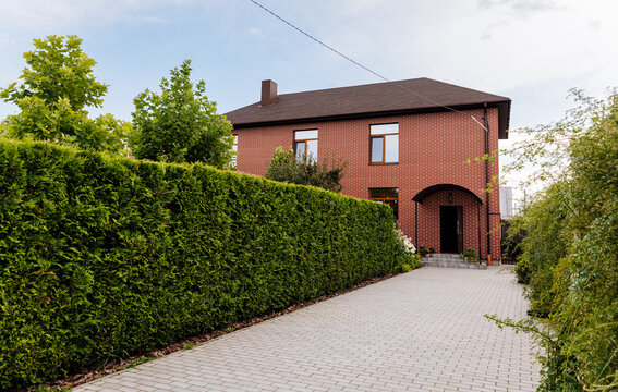 Brick house with long driveway and tall evergreen hedge, suburban residential exterior