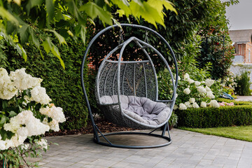 Hanging egg chair on patio in lush garden with hydrangea blooms