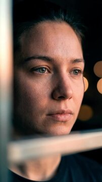 Close up vertical portrait of a thoughtful young woman with detailed skin looking through industrial bars at night for mental health awareness and cinematic urban loneliness storytelling