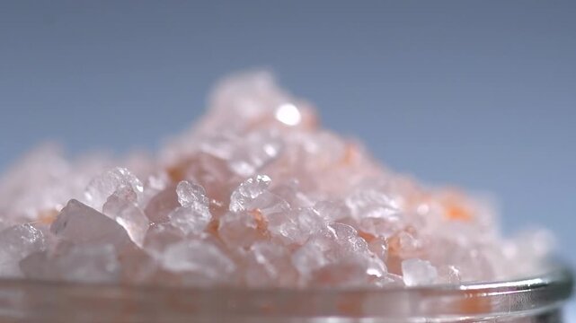 Himalayan salt, pink Himalayan salt crystals close up. Pink coarse salt crystals macro shot, rotating over grey blue background 