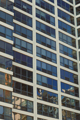 Fototapeta premium City building reflects sunlight in urban setting during daytime with clear sky and visible windows showing different angles of surrounding structure