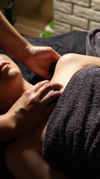 masseuse makes a professional stone massage of the neck, shoulders and chest with black stones. Close-up, relaxation, pleasure. professional massage. Dim light.