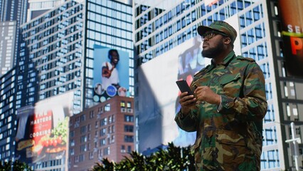 Black military service person browses website on a smartphone in the city center, professional...