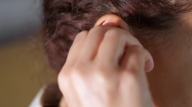 Woman inserting custom molded earplug for noise protection. Close-up view of a woman with curly hair carefully inserting a custom-molded silicone earplug into her ear canal for hearing protection