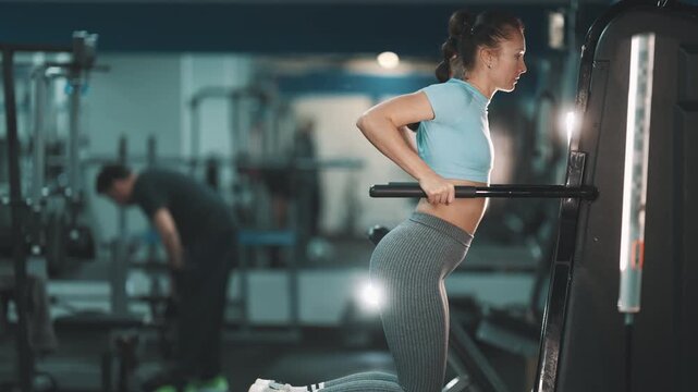 Athletic woman training triceps on dip machine at the gym
