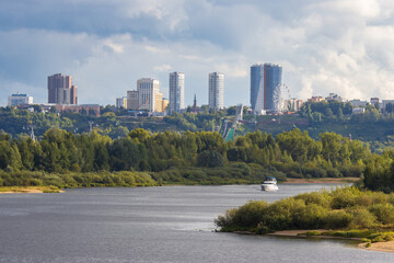 Nizhny Novgorod, Nizhny Novgorod Oblast, Russia. A beautiful summer cityscape. A motor yacht sails along the Vezloma River. Tall modern multi-story residential buildings are visible in the distance.