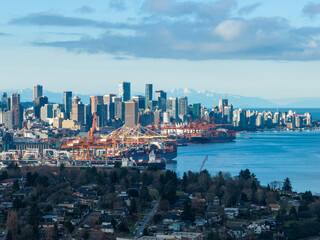 Naklejka premium Vancouver Skyline With Port Cranes Over Water and Mountain Backdrop, A Coastal Cityscape