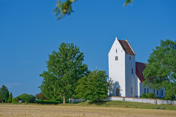 Fototapeta premium White historic church with red roof surrounded by green trees under blue sky