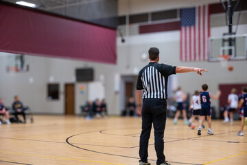 Obraz premium Basketball game in a gym with referee signaling a call during a youth sports event in the afternoon
