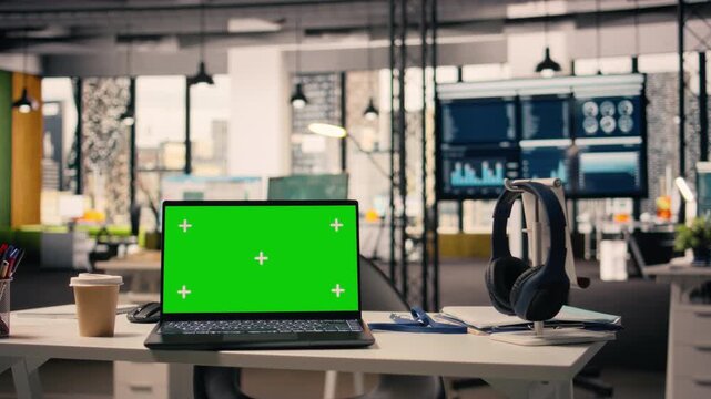 Chroma key screen at empty executive desk with laptop in corporate work environment. Space with modern furniture, decorative details and office supplies, large windows with natural light.