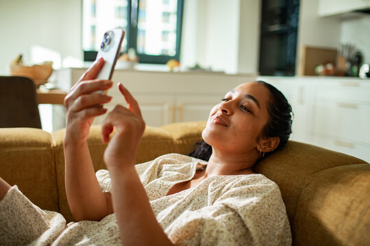 Young woman relaxing on sofa at home using smartphone