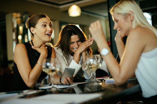 Three businesswomen laughing over drinks in a restaurant
