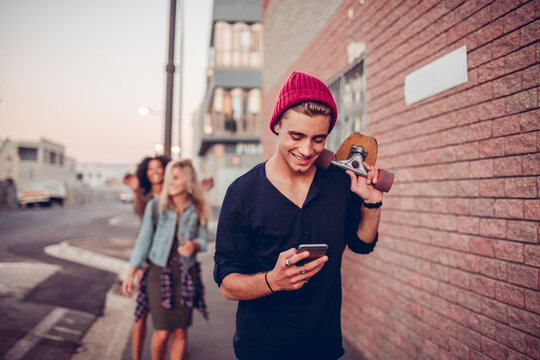 Young man with skateboard texting on urban street