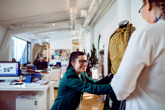 Female fashion designers fitting garment on mannequin in modern studio