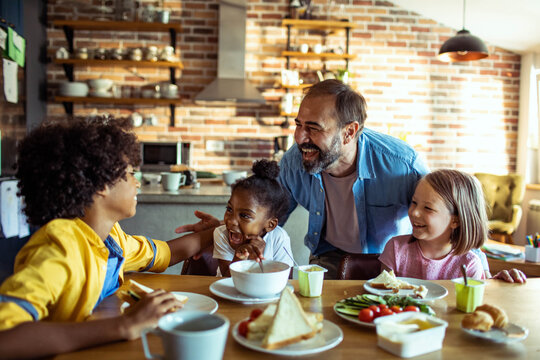 Father and children laughing over breakfast in home kitchen