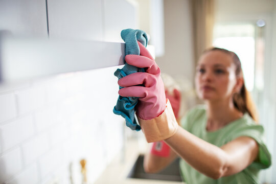 Woman cleaning kitchen cabinet with microfiber cloth at home