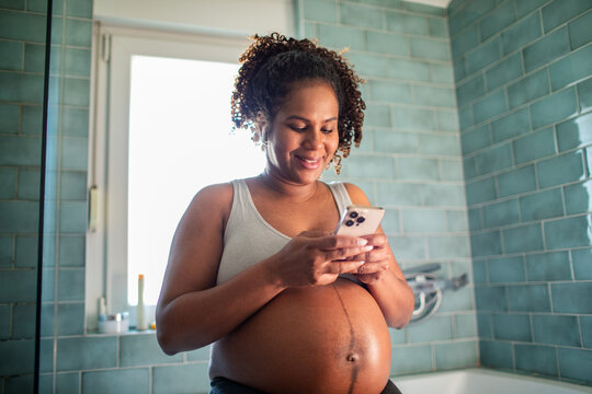 Pregnant woman checking smartphone in home bathroom