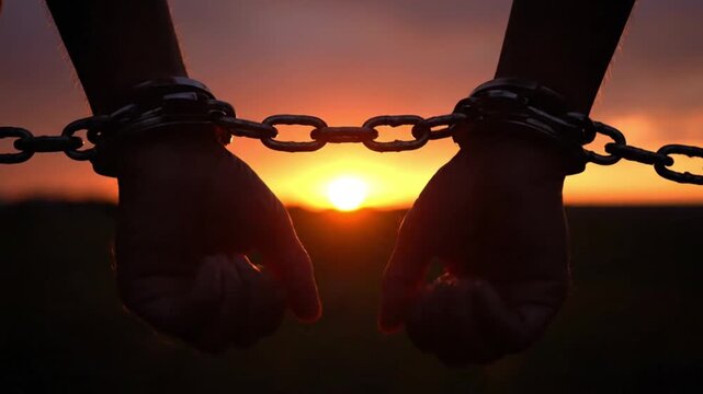 Silhouetted hands bound by heavy chains against a dramatic sunset, symbolizing the profound human struggle for freedom and liberation from oppression