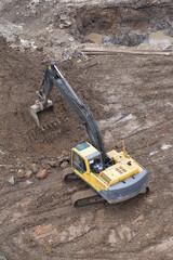 A yellow hydraulic excavator is digging into a pile of dirt on a muddy construction site. Concept of earthworks and site preparation. © Helga P-A.
