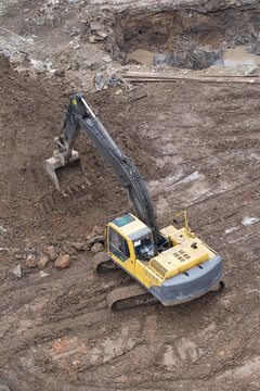 A yellow hydraulic excavator is digging into a pile of dirt on a muddy construction site. Concept of earthworks and site preparation.