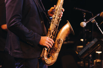 Naklejka premium Concert view of saxophonist musician, saxophone sax player with vocalist and musical band during jazz orchestra show performing music on a stage in the scene lights, concert in a musical club hall