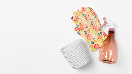 Gardening tools set with floral gloves, spray bottle and ceramic plant pot on white background. Top view, copy space