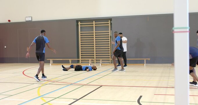 Diverse male volleyball players diving for ball on court, assessing injured teammate, lifting him