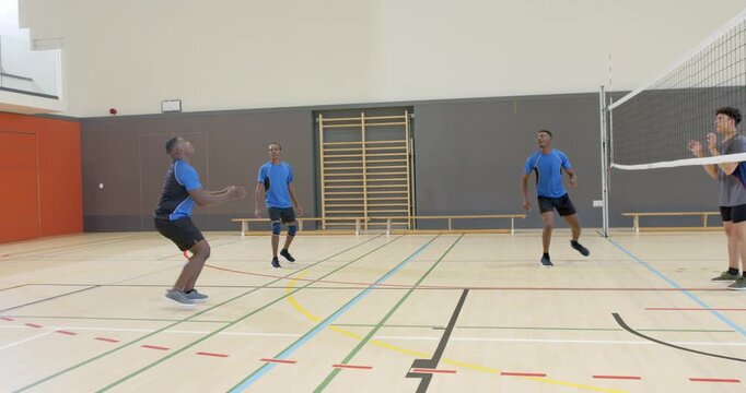 Incoming ball Diverse male team in gym passing spiking over net toward rival bracing reception