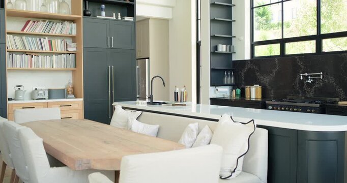 Camera is panning right and forward in kitchen, revealing wooden dining table island to show layout