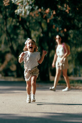 Obraz premium A joyful child running outdoors in a park under sunlight with an adult watching from a distance creating a fun and lively moment of carefree play.