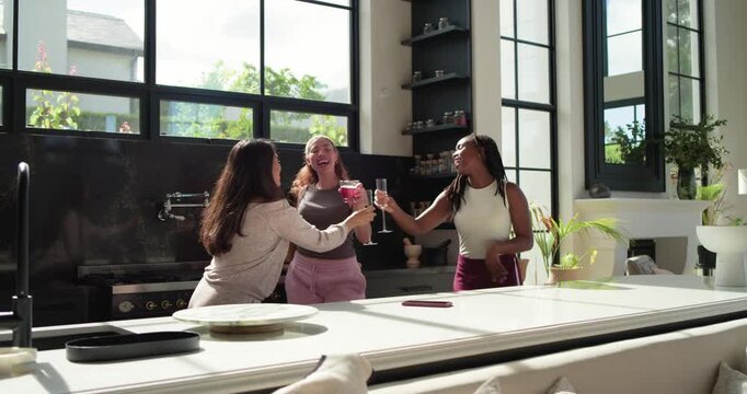 African American women friends dancing, clinking wine glasses at kitchen island while music playing
