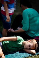 Fototapeta premium Young girl sleeping outdoors on a blanket during a family gathering under the sun